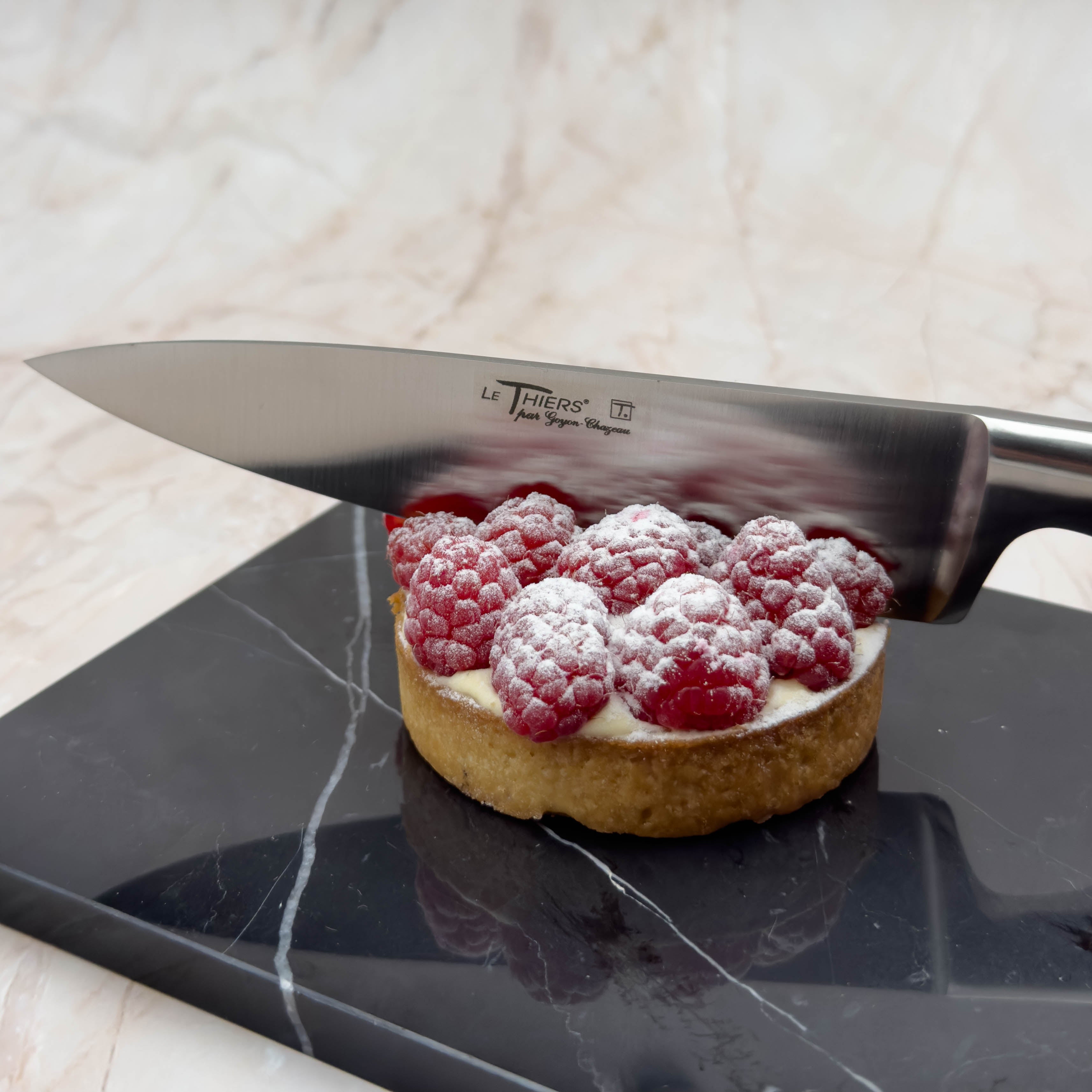 French knife cutting raspberry pie on marble